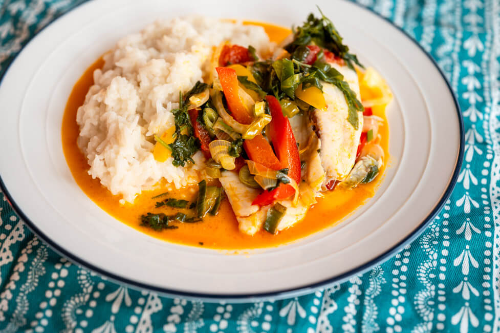 Moqueca de peixe mit Reis auf weißem Teller angerichtet auf blauem Tischtuch