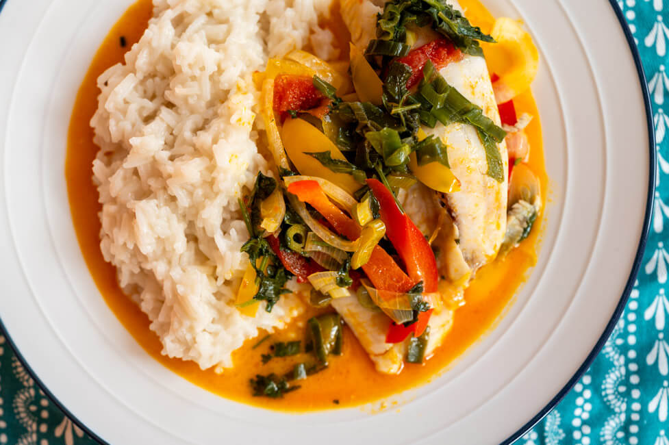 Moqueca de peixe mit Reis auf weißem Teller angerichtet auf blauem Tischtuch