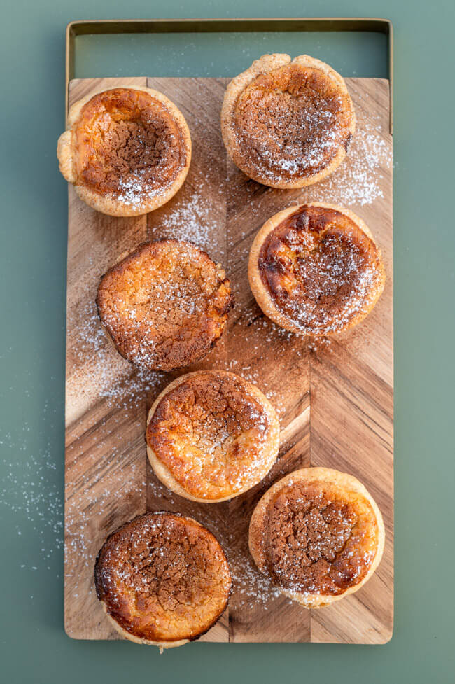 Pasteis de Nata auf Holzbrett und grünem Untergrund