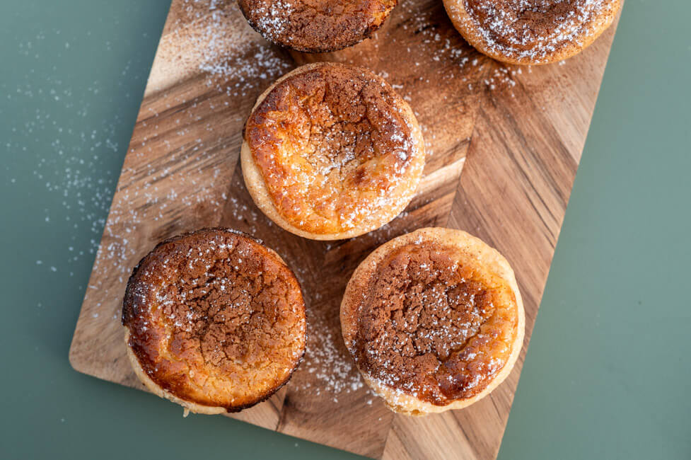 Pasteis de Nata auf Holzbrett und grünem Untergrund