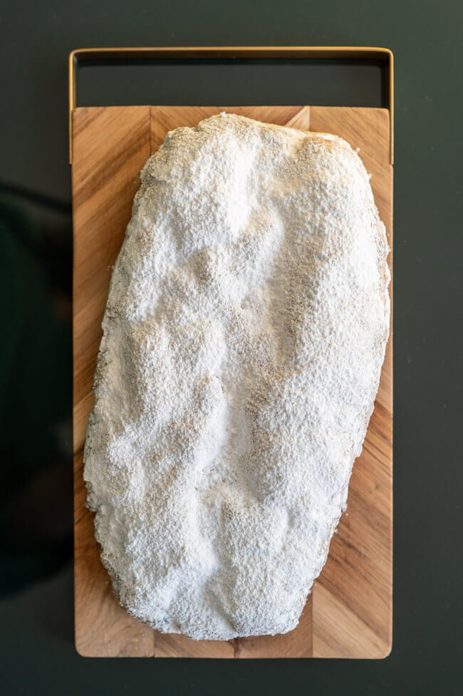 Ein Stück Aprikosen-Stollen mit Pinienkernen und Rosmarin auf Holzbrett aufgeschnitten.