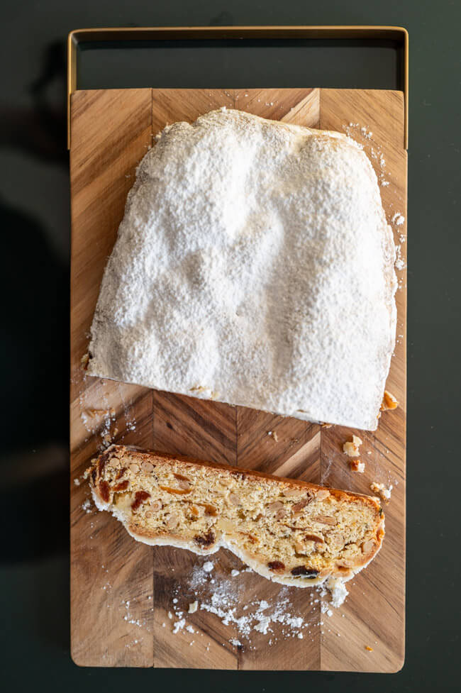 Ein Stück Aprikosen-Stollen mit Pinienkernen und Rosmarin auf Holzbrett aufgeschnitten.