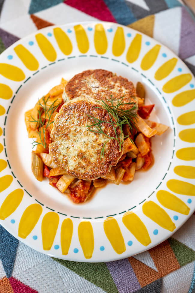 Putenfrikadellen auf Fenchel-Tomaten-Gemüse und buntem Keramikteller.