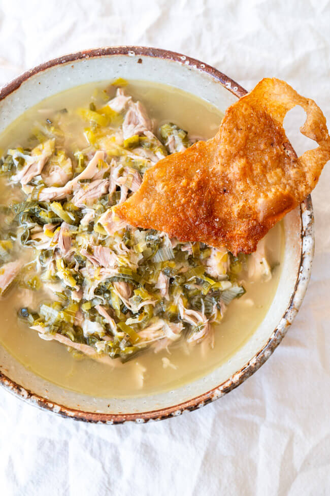Ein Teller mit Hühner-Lauch-Suppe und einem Stück knuspriger Haut on top.
