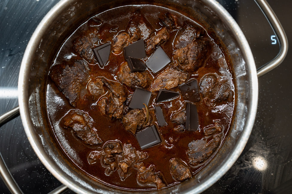 Geschmorte Hirschbacken in Sauce im Topf mit Schokoladenstücken
