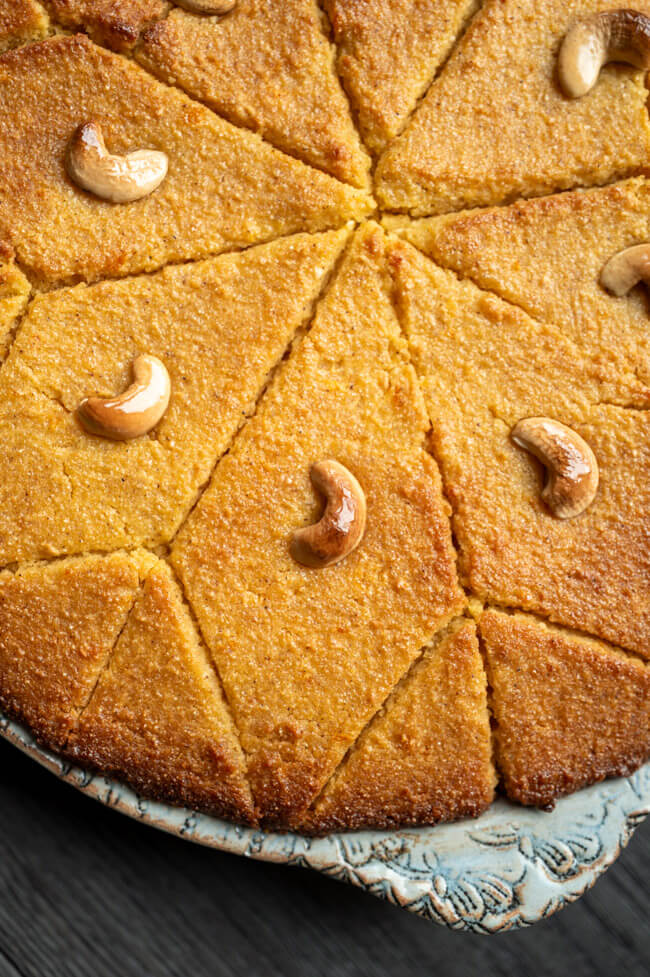 Orangen-Grießkuchen mit Cashewkernen dekoriert in hellblauer Keramikform auf dunklem Untergrund.
