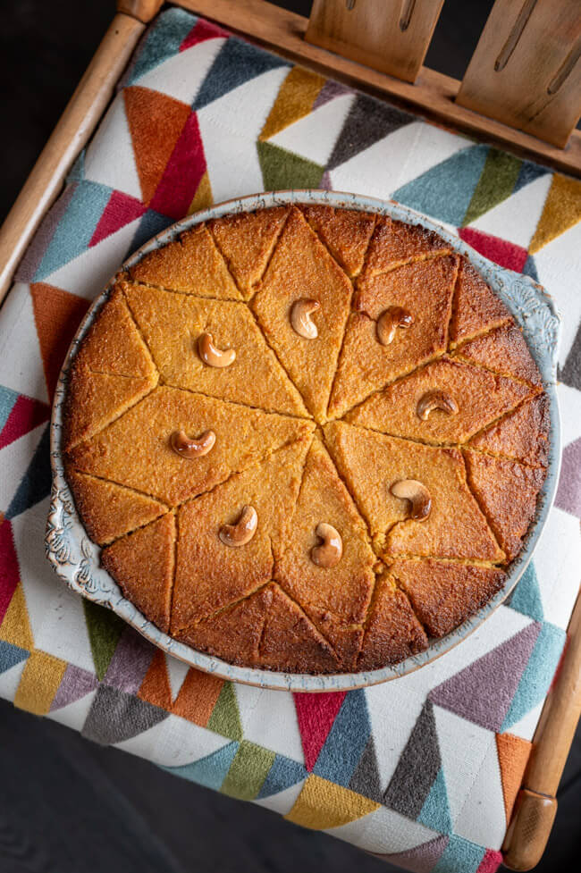 Orangen-Grießkuchen mit Cashewkernen dekoriert in hellblauer Keramikform auf buntem Untergrund.