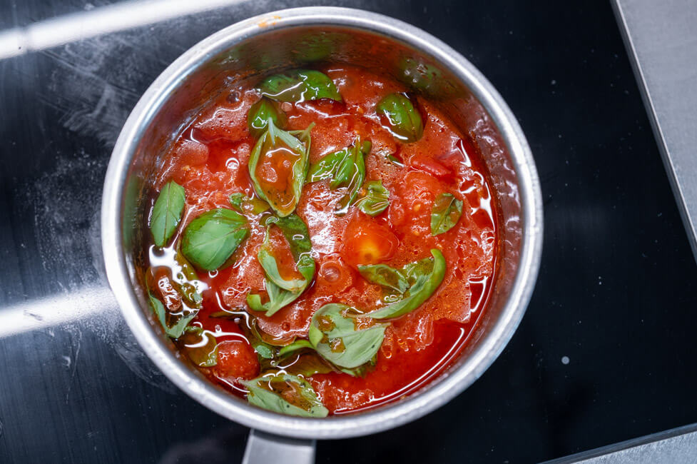 Tomatensoße für die Ravioli kocht im Topf mit frischem Basilikum