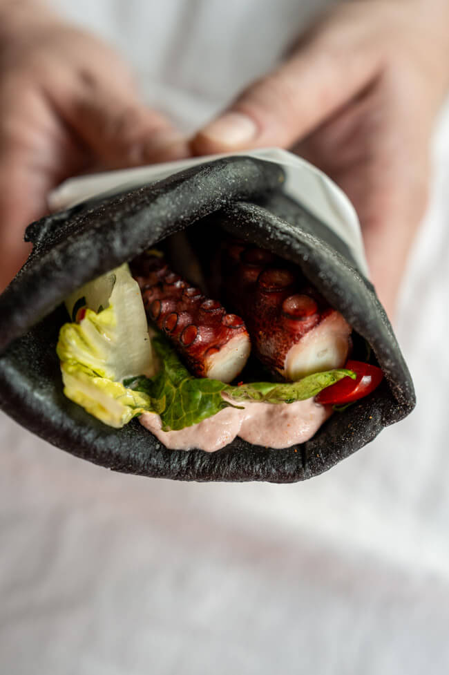 Hände halten Sepia-Pita mit Creme Tarama und gegrilltem Oktopus