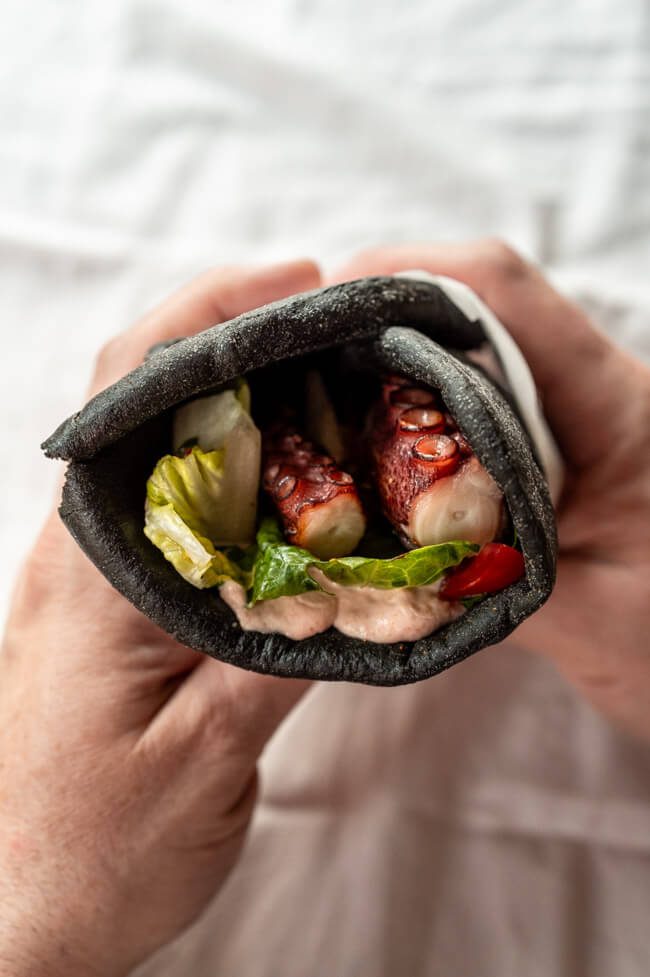 Hände halten Sepia-Pita mit Creme Tarama und gegrilltem Oktopus