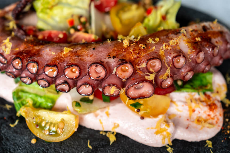 Sepia-Pita mit Creme Tarama und gegrilltem Oktopus auf Butterbrotpapier und Holzbrett angerichtet