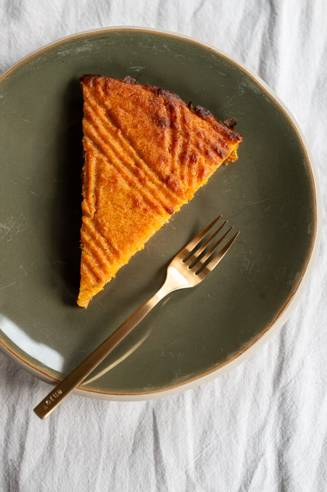 Ein Stück Süßkartoffelkuchen auf grünem Teller mit goldener Gabel auf weißer Tischdecke