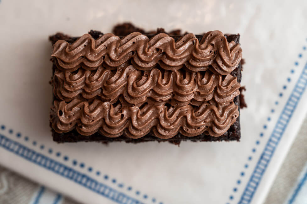 Ein Stück Gewürzkuchen mit Schokoladenbuttercreme auf weißem Keramiktablett