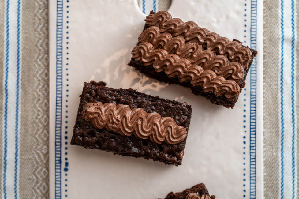 Stücke Gewürzkuchen mit Schokoladenbuttercreme auf weißem Keramiktablett und gestreifter Tischdecke