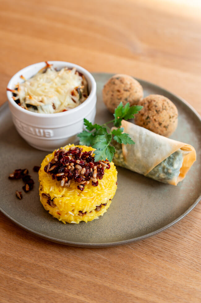 Gemischte Mezze, bestehend aus Tahchin mit Börek, Moussaka und Falafel auf grünem Teller