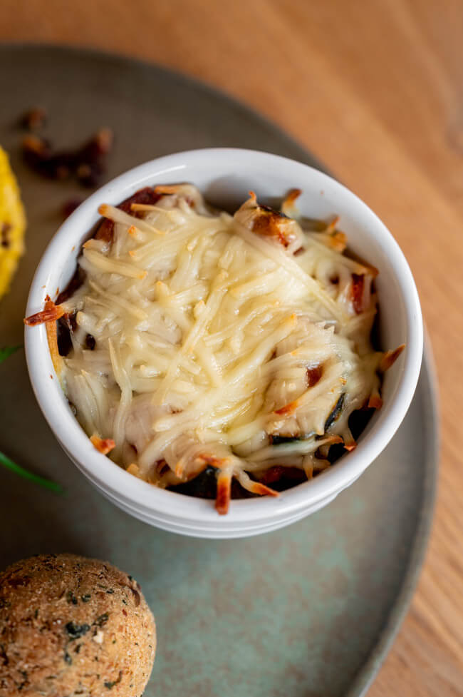 Moussaka in weißem Keramikförmchen auf grünem Keramikteller