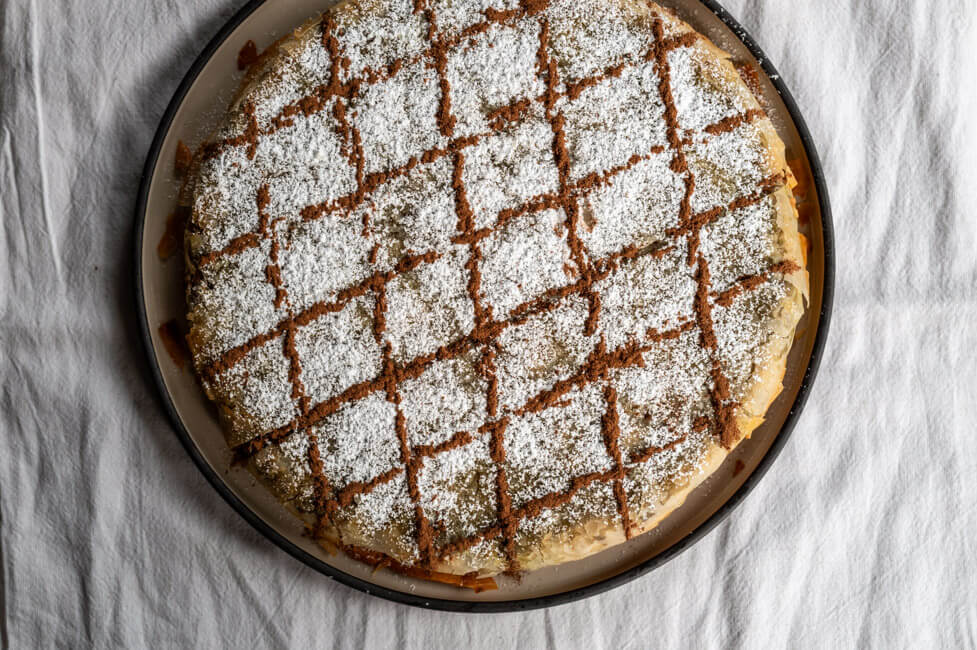 Fertig gebackene Pastilla, verziert mit Puderzucker und Zimt auf Keramikteller und weißer Tischdecke
