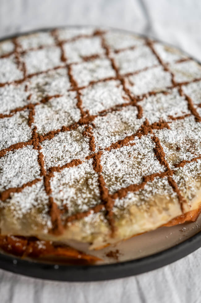 Fertig gebackene Pastilla, verziert mit Puderzucker und Zimt auf Keramikteller und weißer Tischdecke