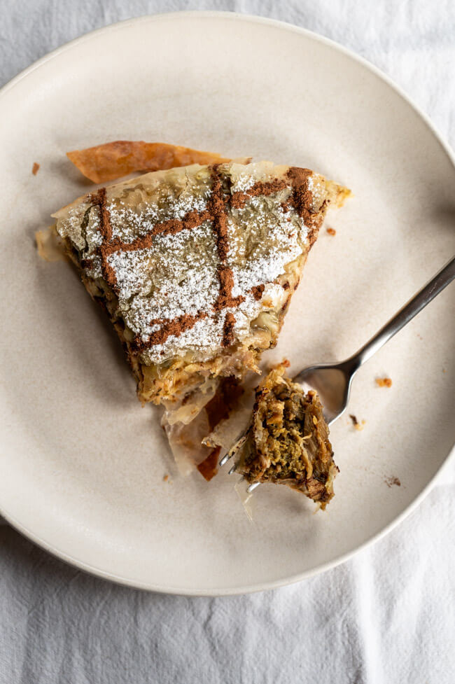 Ein Stück Pastilla, verziert mit Puderzucker und Zimt, auf Keramikteller und weißer Tischdecke