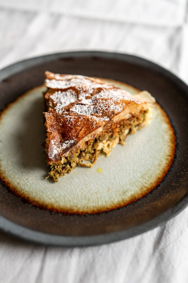 Ein Stück Pastilla, verziert mit Puderzucker und Zimt, auf Keramikteller und weißer Tischdecke