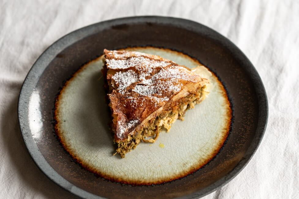 Ein Stück Pastilla, verziert mit Puderzucker und Zimt, auf Keramikteller und weißer Tischdecke