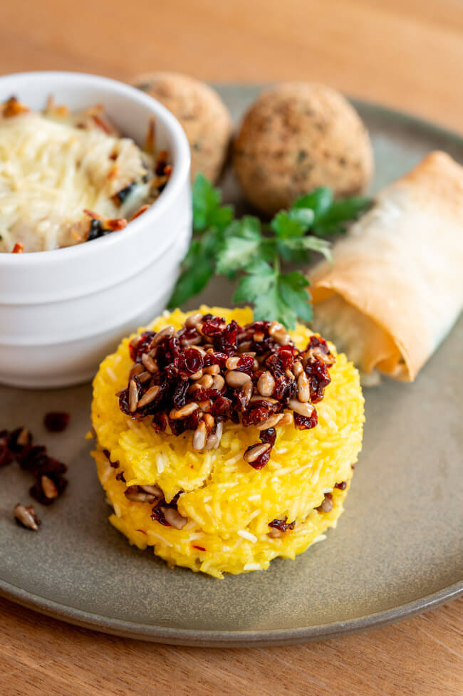 Tahchin mit Berberitzen-Sonnenblumenkern-Topping mit den anderen Mezze auf grünem Porzellanteller
