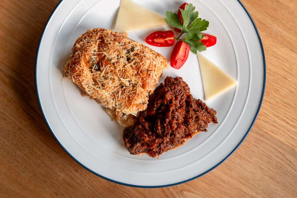 Weißer Teller mit einer Portion Zuppa Gallurese und Ghisatu, garniert mit Tomaten, Petersilie und Provolone Käse