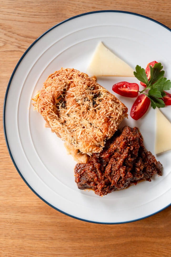 Weißer Teller mit einer Portion Zuppa Gallurese und Ghisatu, garniert mit Tomaten, Petersilie und Provolone Käse