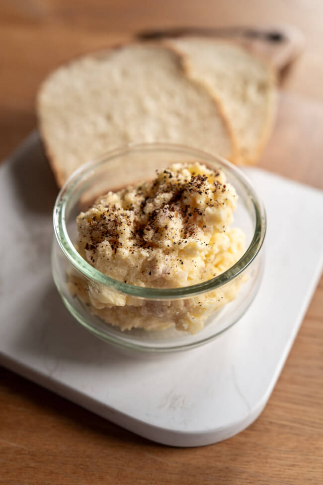 Erdäpfelkäs in Glasschälchen mit zwei Scheiben Buttermilchbrot auf Holz-Marmor-Brett