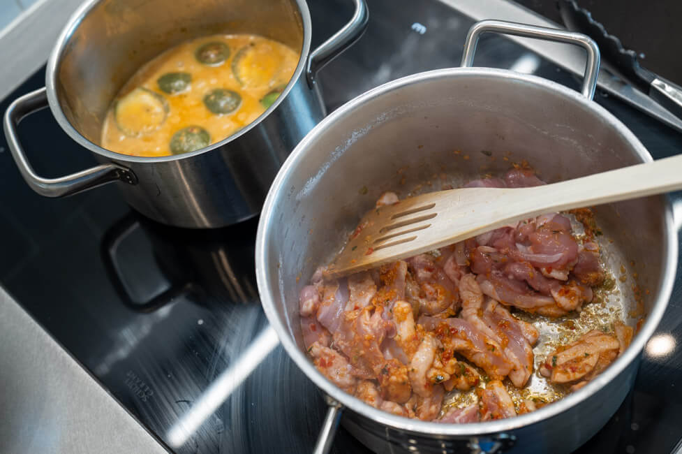 Hähnchenschenkelfleisch wird mit roter Currypaste im Topf angeröstet