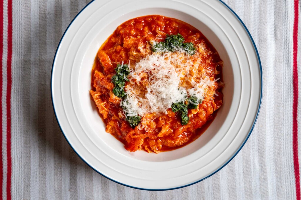 Weißer Teller mit einer Portion Trippa alla parmigiana, getoppt mit Kräuteröl und frisch geriebenem Parmesan