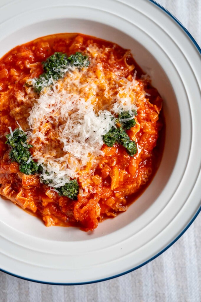 Weißer Teller mit einer Portion Trippa alla parmigiana, getoppt mit Kräuteröl und frisch geriebenem Parmesan