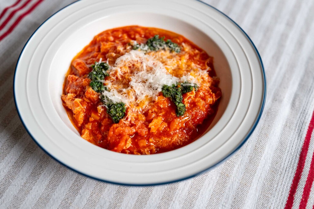 Weißer Teller mit einer Portion Trippa alla parmigiana, getoppt mit Kräuteröl und frisch geriebenem Parmesan
