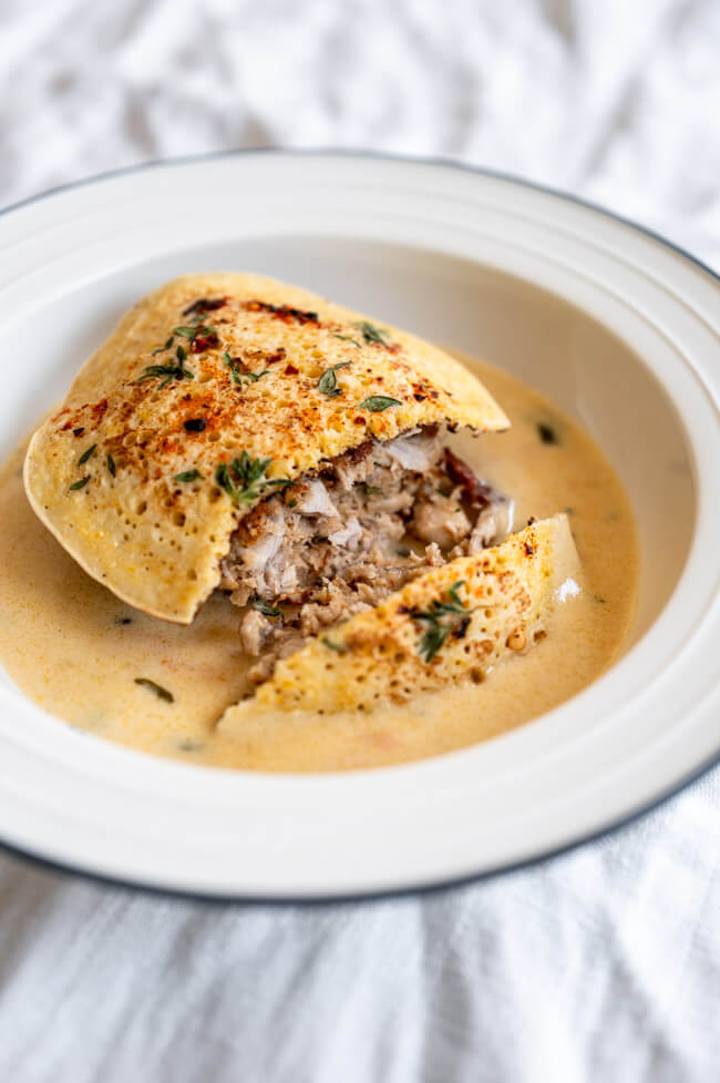 Kaninchen-Frikadelle mit Polenta-Pfannkuchen angeschnitten auf Meerrettich-Rahmsauce in weißem Teller mit blauem Rand