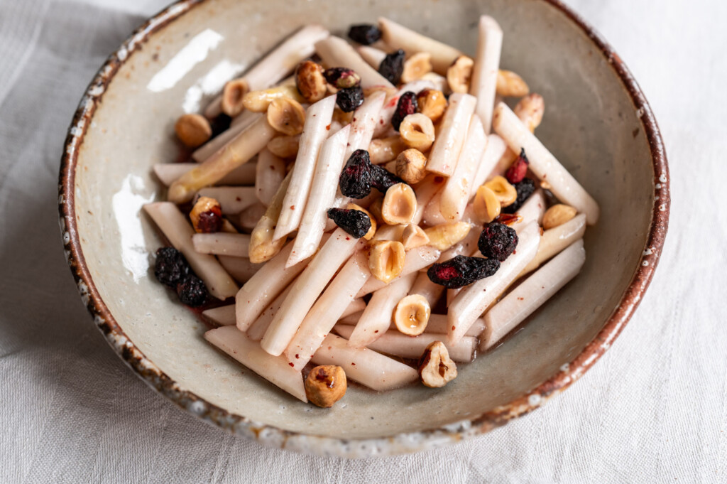 Spargelsalat mit Haselnüssen und Haskap-Beeren angerichtet auf Keramikteller.