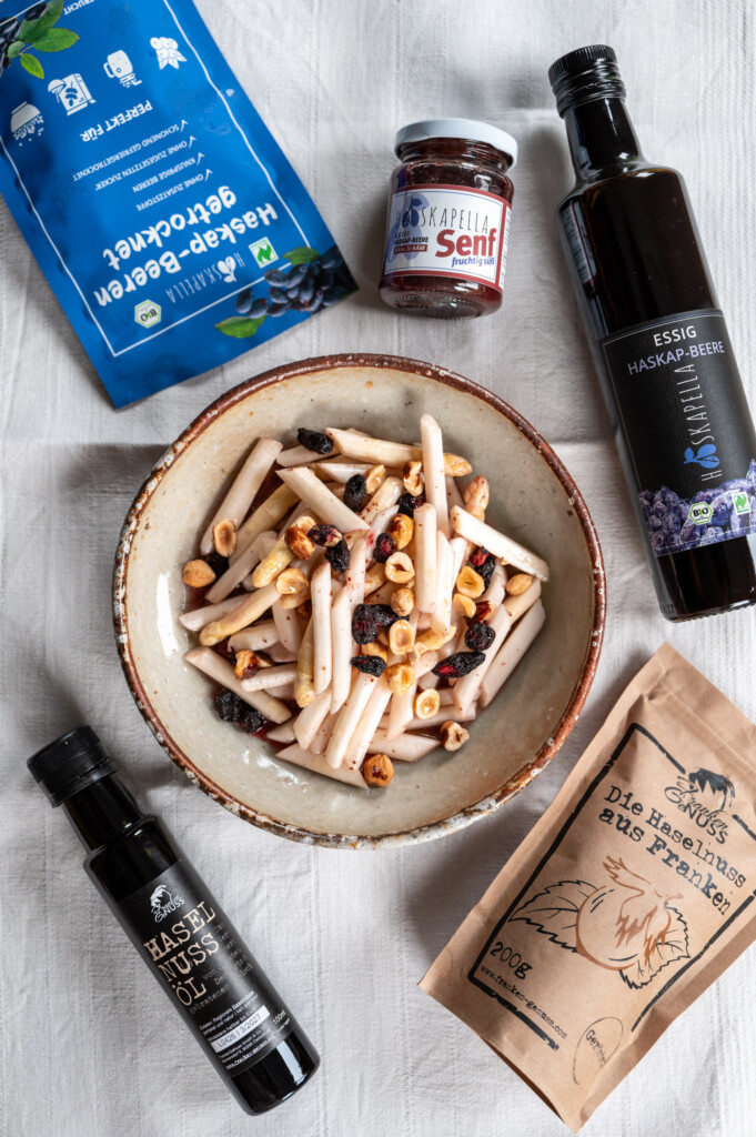 Spargelsalat mit Haselnüssen und Haskap-Beeren angerichtet auf Keramikteller mit Haskapella Essig, gefriergetrockneten Haskapbeeren, Haskapella Senf, Haselnüssen und Haselnussöl von Franken GeNuss.