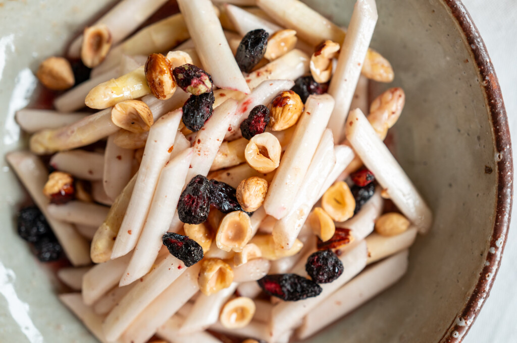 Spargelsalat mit Haselnüssen und Haskap-Beeren angerichtet auf Keramikteller.