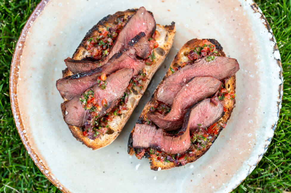 Zwei Scheiben geröstetes Weißbrot mit Oliven-Caponata und gegrilltem Wagyu auf Keramikteller