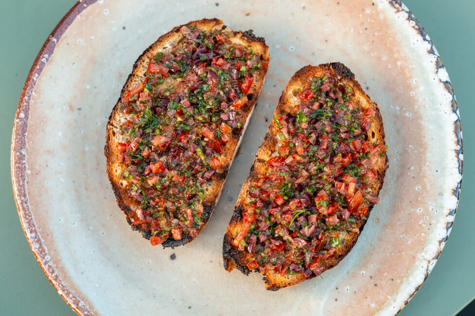 Zwei Scheiben geröstetes Weißbrot mit Oliven-Caponata auf Keramikteller