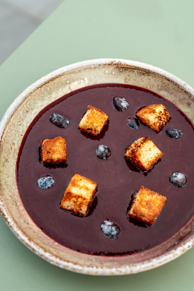 Haskap-Beeren Gazpacho mit Brioche auf grünem Untergrund