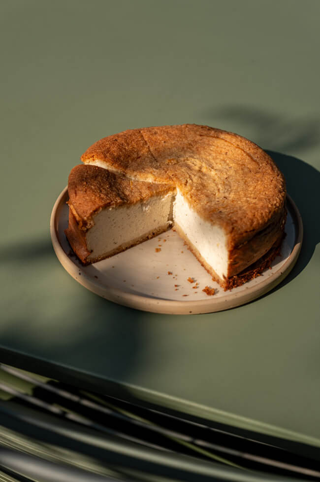 Angeschnittener Haselnuss-Käsekuchen mit Skyr auf Teller angerichtet auf grünem Tisch im Sonnenlicht