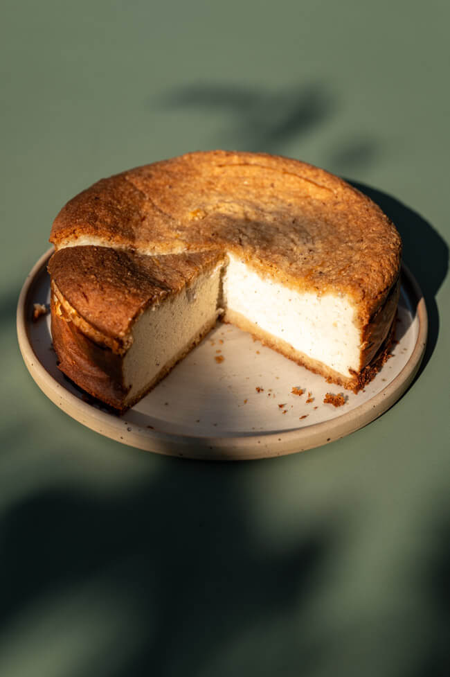 Angeschnittener Haselnuss-Käsekuchen mit Skyr auf Teller angerichtet auf grünem Tisch im Sonnenlicht